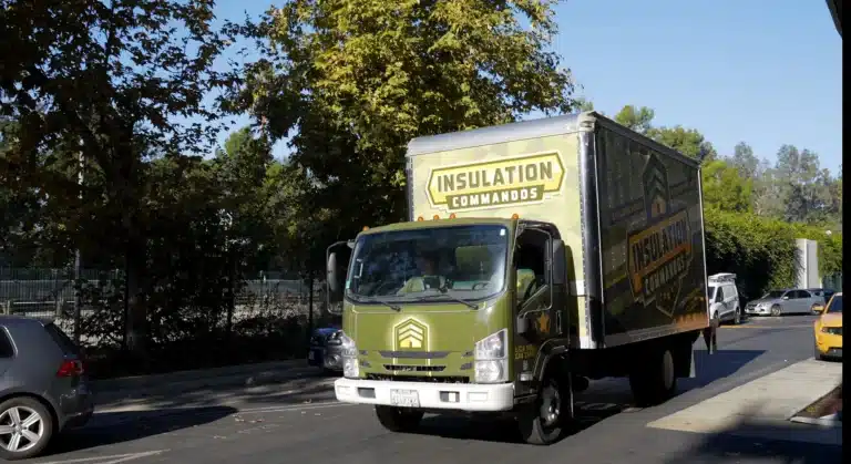 Green Insulation Commandos truck driving on a residential street.