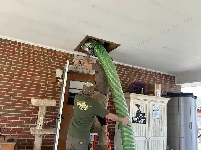 Insulation Commandos technicians blowing insulation into an attic through a ceiling access hatch to improve home energy efficiency.
